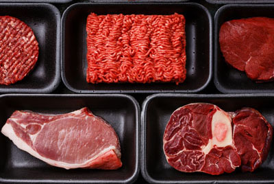Various raw, red meat products lined up in open black Styrofoam containers.