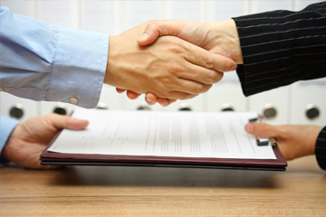 Two people shaking hands over documents.