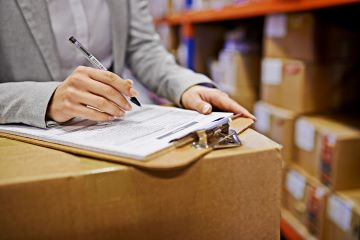 hand holding pen and clip board on top of box