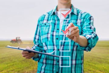 Person standing in field holding a clipboard and checking off check boxes.