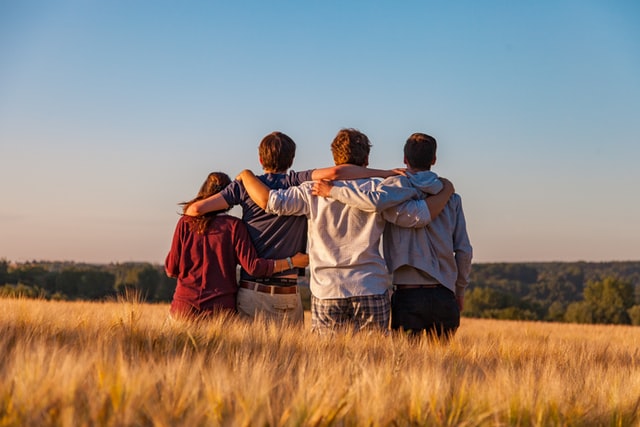 Four people standing in wheat field with arms on each others' shoulders