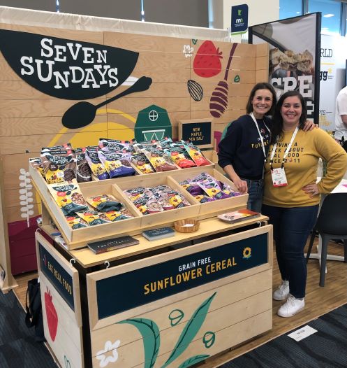 two exhibitors standing next to the Seven Sundays grain-free sunflower cereal display
