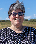 short-haired woman wearing glasses standing in a pasture