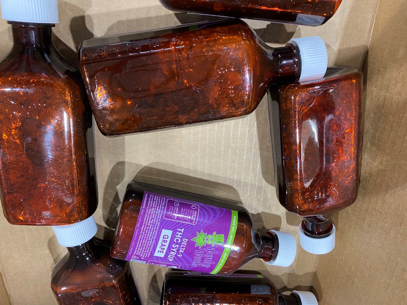 Several bottles of Wonky Weeds-brand grape-flavored delta 9 THC syrup with visible mold growth in the bottles.