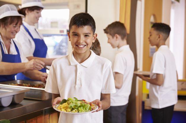 boy holding lunch tray with servers in background