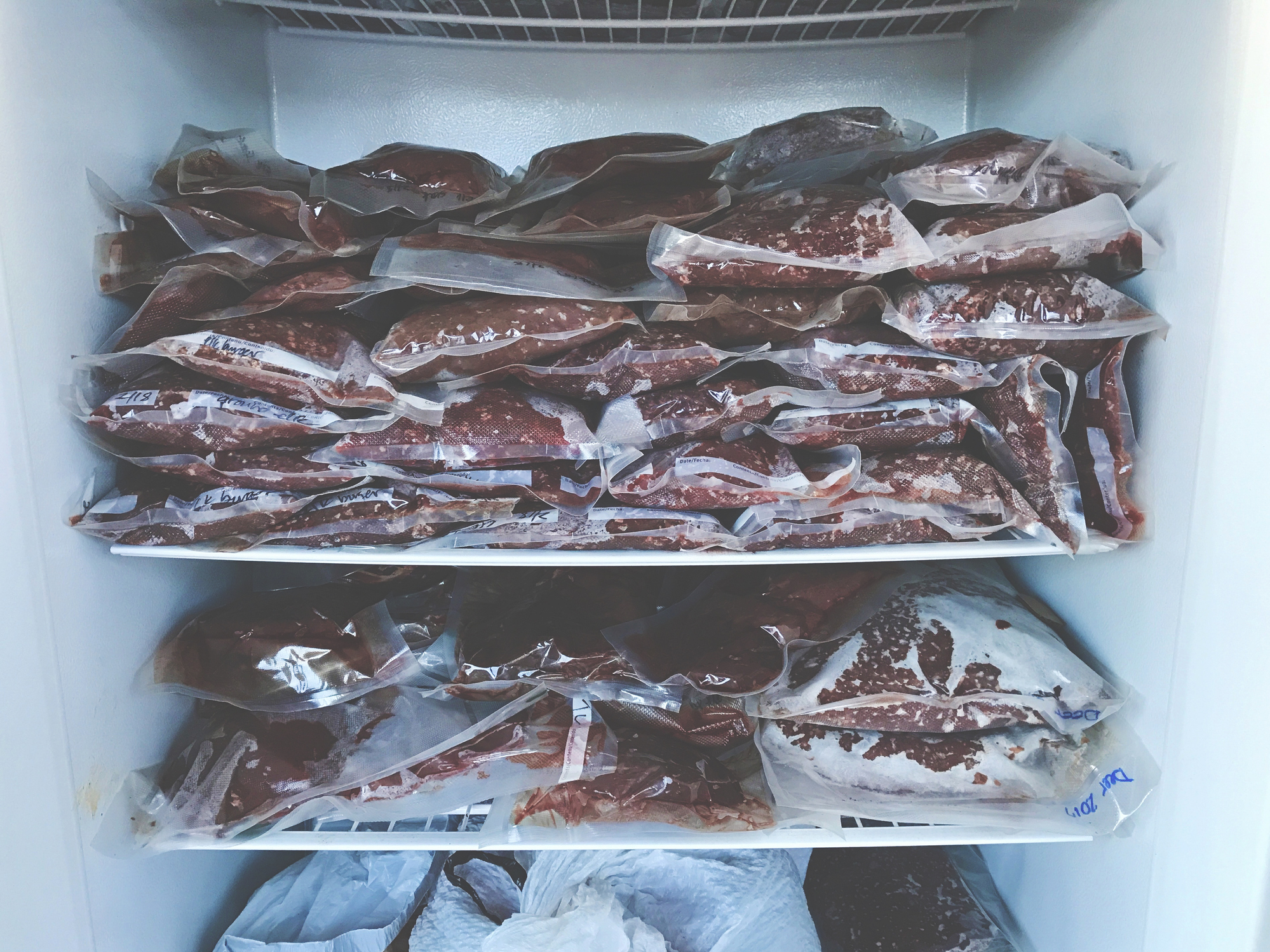 Packages of ground wild game meat are stacked on shelves in a freezer