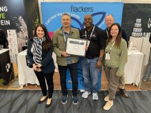 Five people holding a certificate in front of tradeshow exhibit